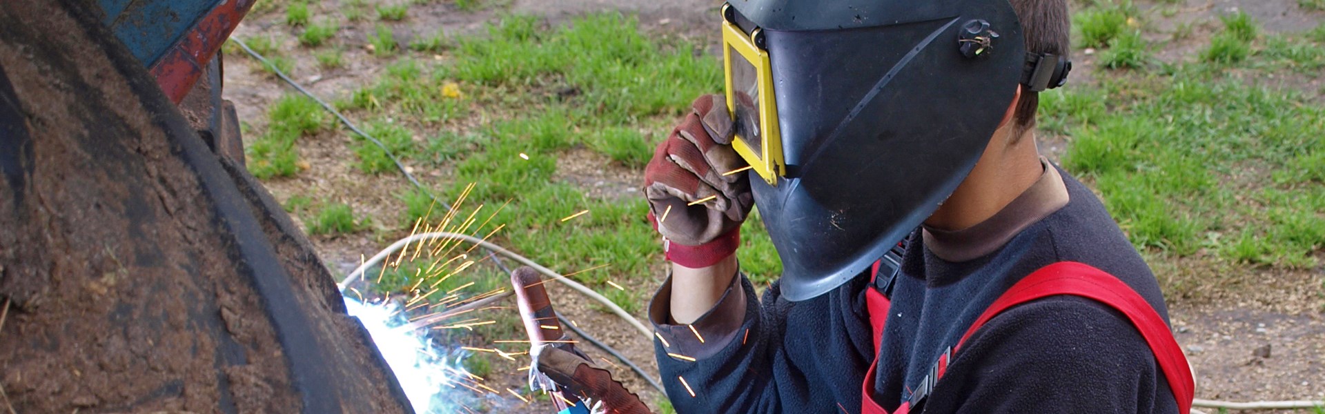 Male wearing welding mask welding the back of a tractor on a farm