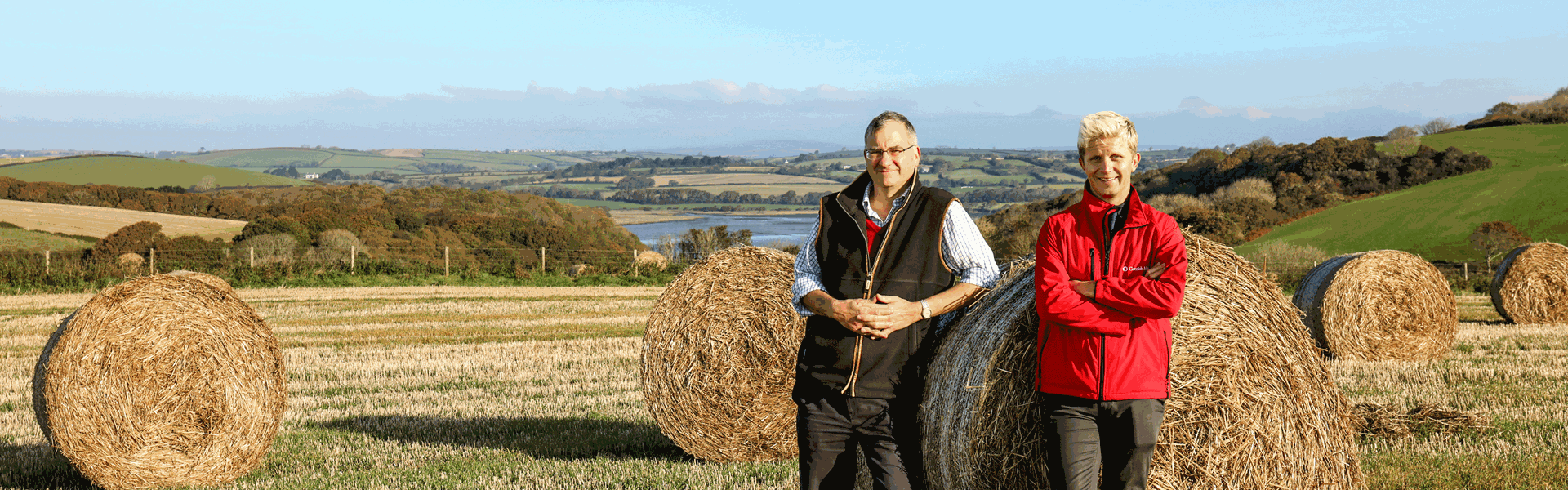 Farming Member With Insurance Advisor standing next on Hay Bales