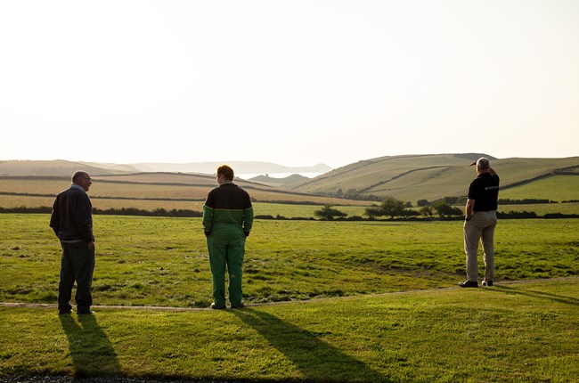 Three men standing in field together looking at sea view