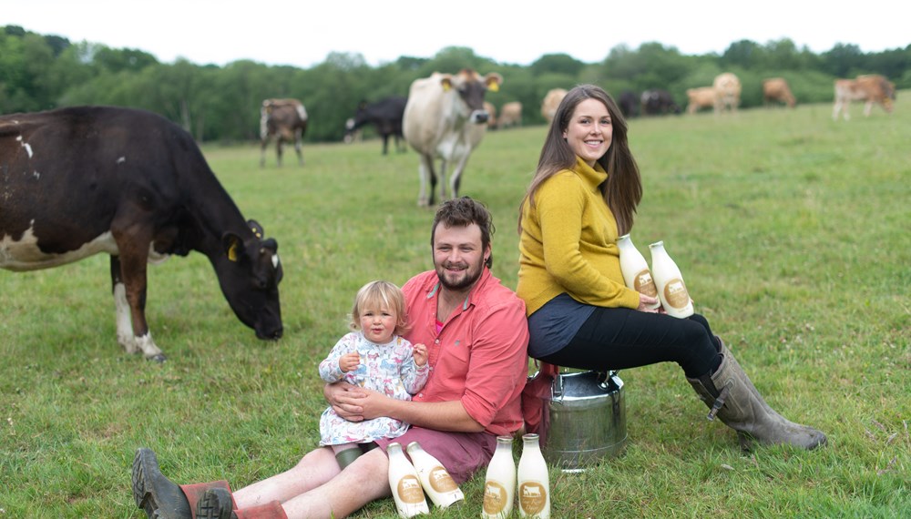 Sam Bullingham and Kate Bray with Daughter Sat in Field With Cows In The Background