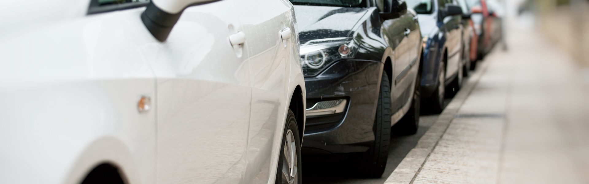 Several cars parked alongside a pavement in a residential area
